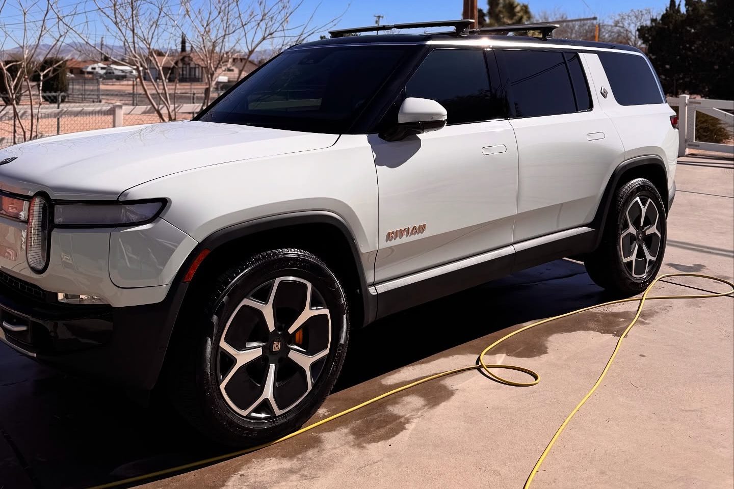 A white Rivian R1S parked in a driveway after a detail, hose coiled alongside