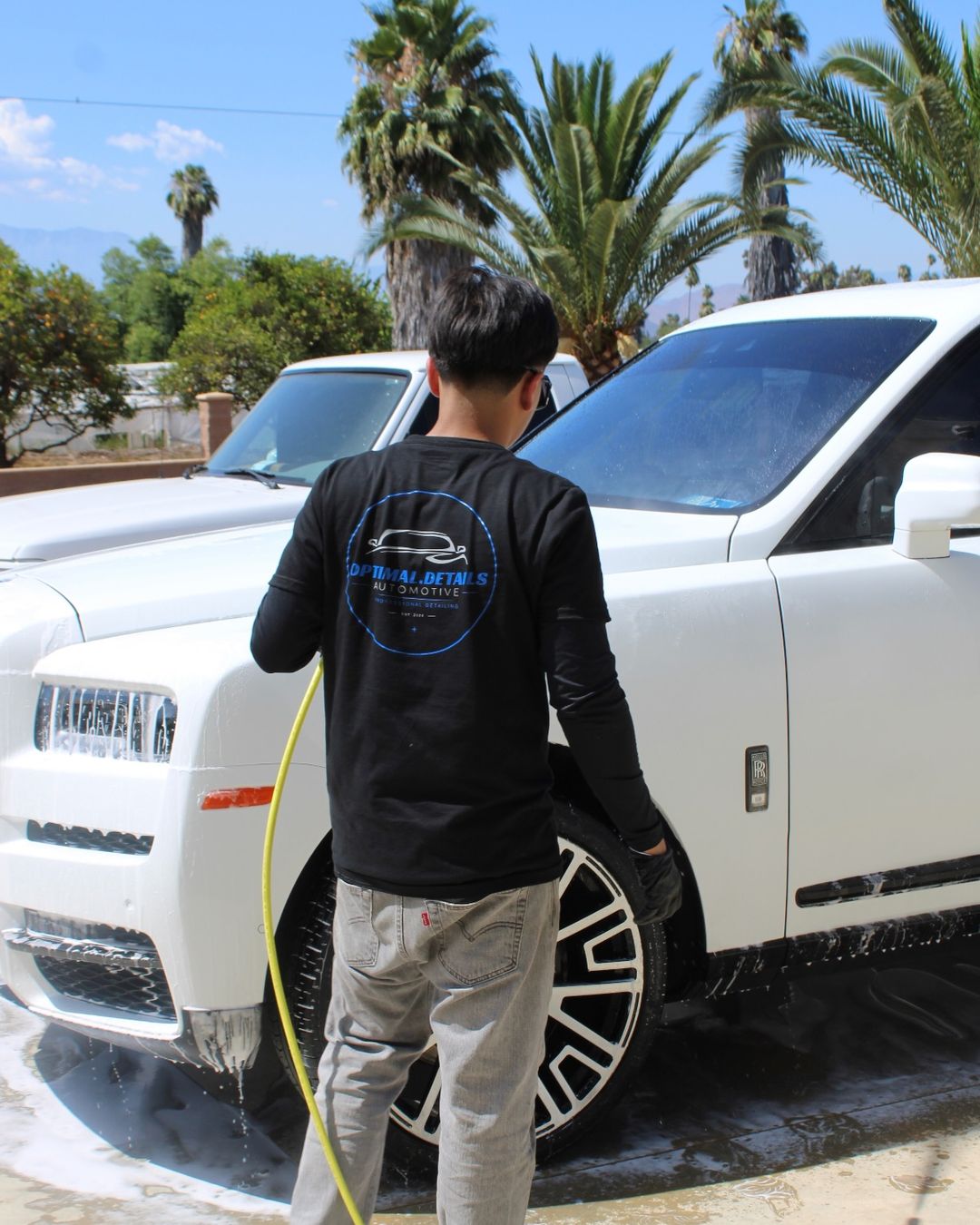 Jayden washing a white Rolls-Royce Cullinan in the Optimal Details shirt