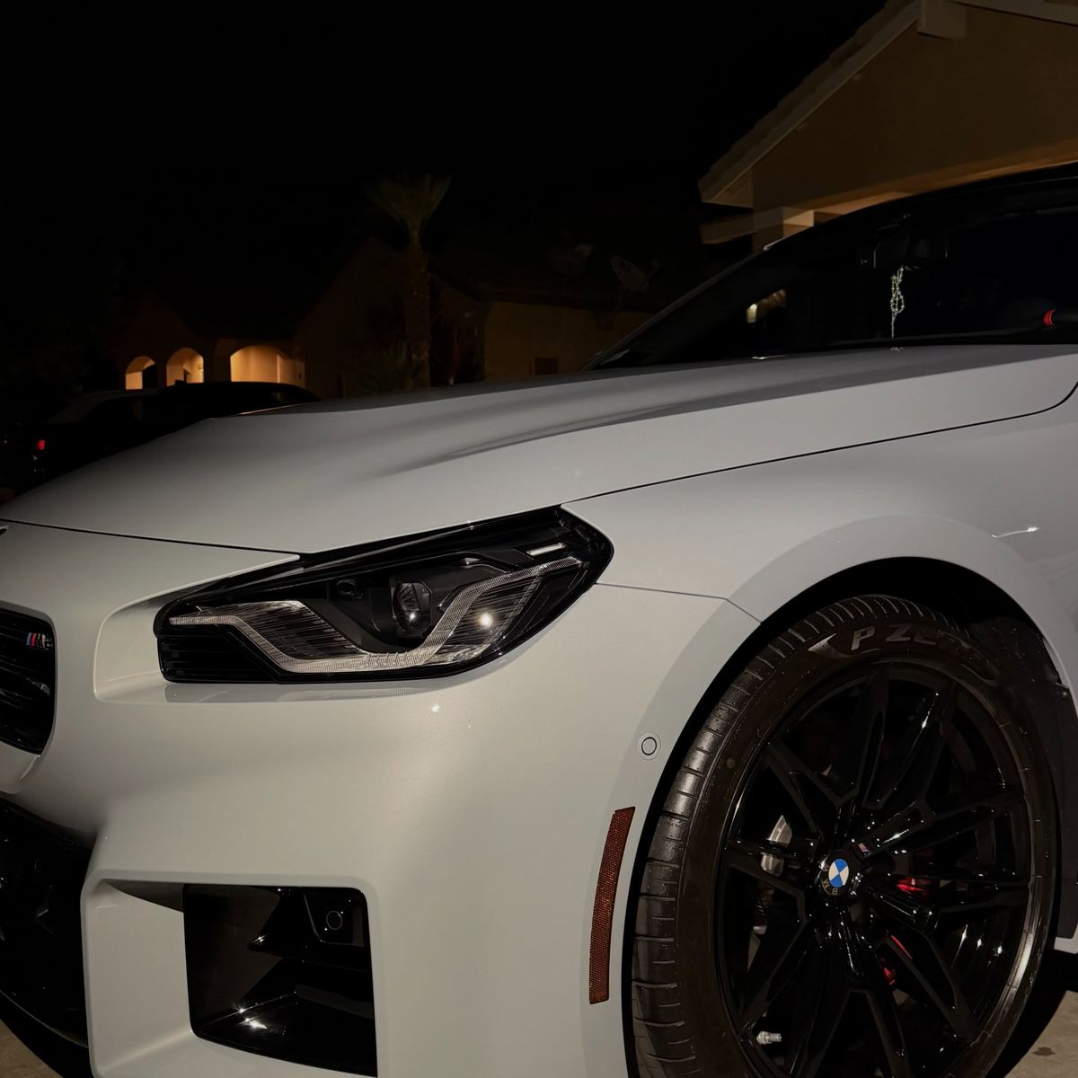 A white BMW M2 at night, paint reflecting the lights cleanly
